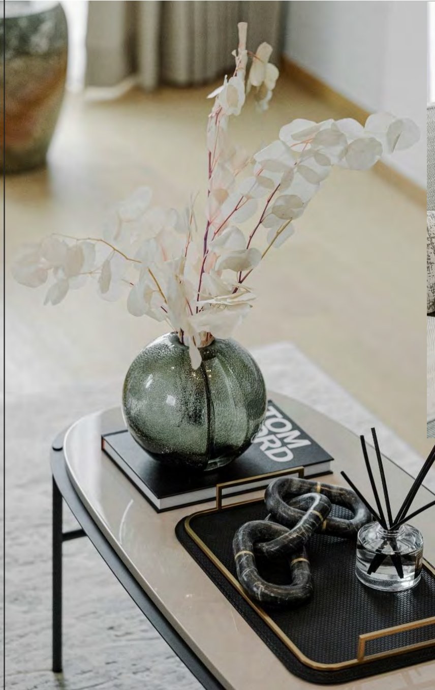 รายละเอียดบนโต๊ะกลาง แจกันแก้วสีชาใส่ยูคาลิปตัสสีขาว หนังสือดีไซน์วางซ้อน วัตถุหินอ่อนทรงโซ่ และก้านไม้หอม