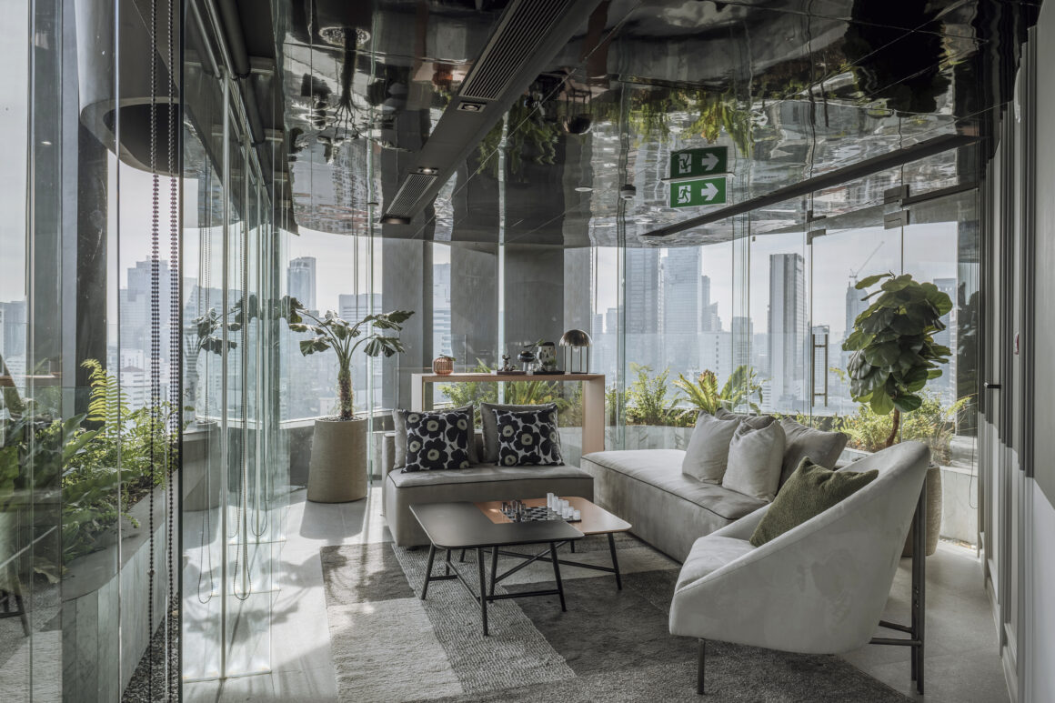 sky lounge ผนังกระจกรอบด้าน โซฟาสีครีม หมอนอิงลวดลาย ต้นไม้เขียวชอุ่ม ฝ้าเพดานกระจกเงา และวิวเส้นขอบฟ้ากรุงเทพแบบพาโนรามา