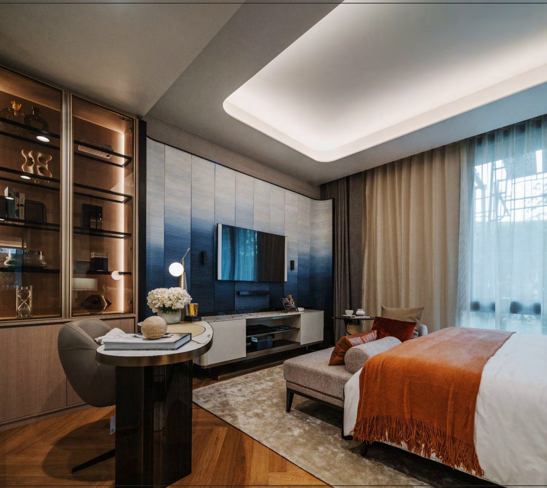 ห้องนอนใหญ่พร้อมผนังบุแผงไล่เฉดสีน้ำเงิน ผ้าคลุมเตียงสีสนิม ตู้โชว์บานกระจก และโต๊ะเขียนหนังสือท็อปหินอ่อน
