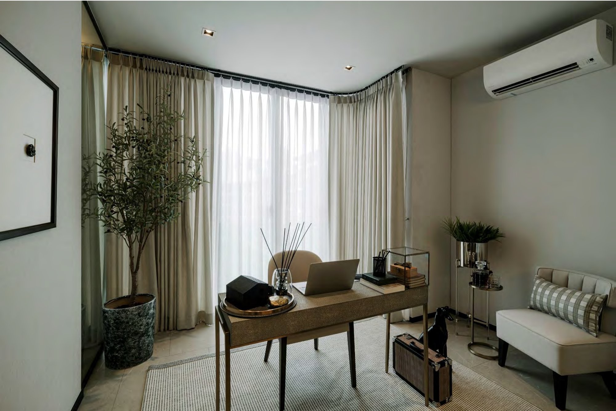 ห้องทำงานในบ้านขนาดกะทัดรัด โต๊ะทำงานหุ้มหนัง shagreen แล็ปท็อป ต้นมะกอกในกระถาง และเก้าอี้ทรงเตี้ยข้างหน้าต่างมุมห้องที่กรุด้วยผ้าม่านโปร่ง