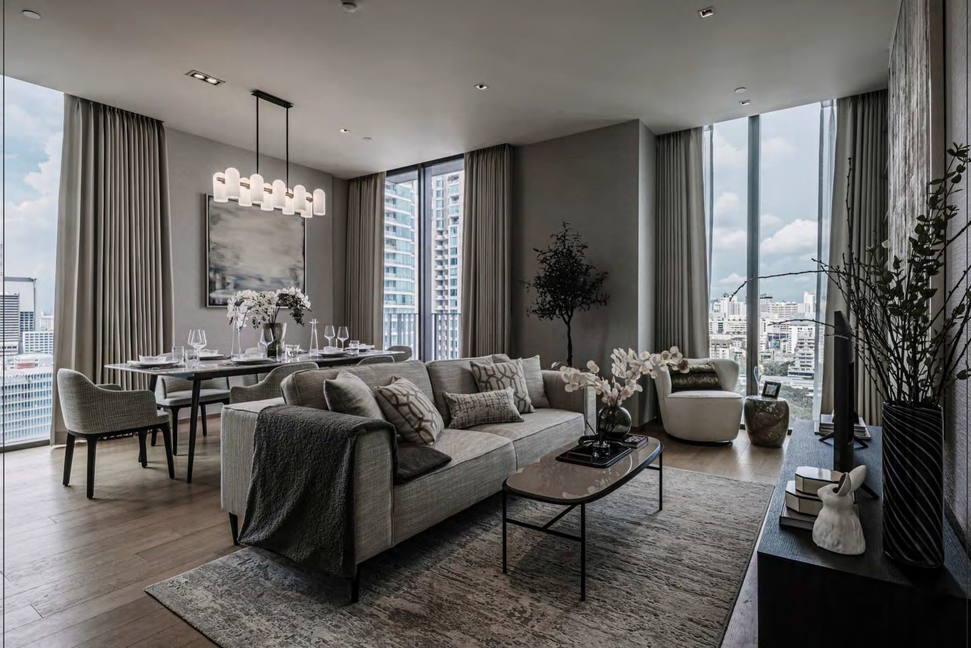 Open-plan living room in soft greys with linen sofa, tubular opaline pendant, dining table and floor-to-ceiling windows framing the Bangkok skyline