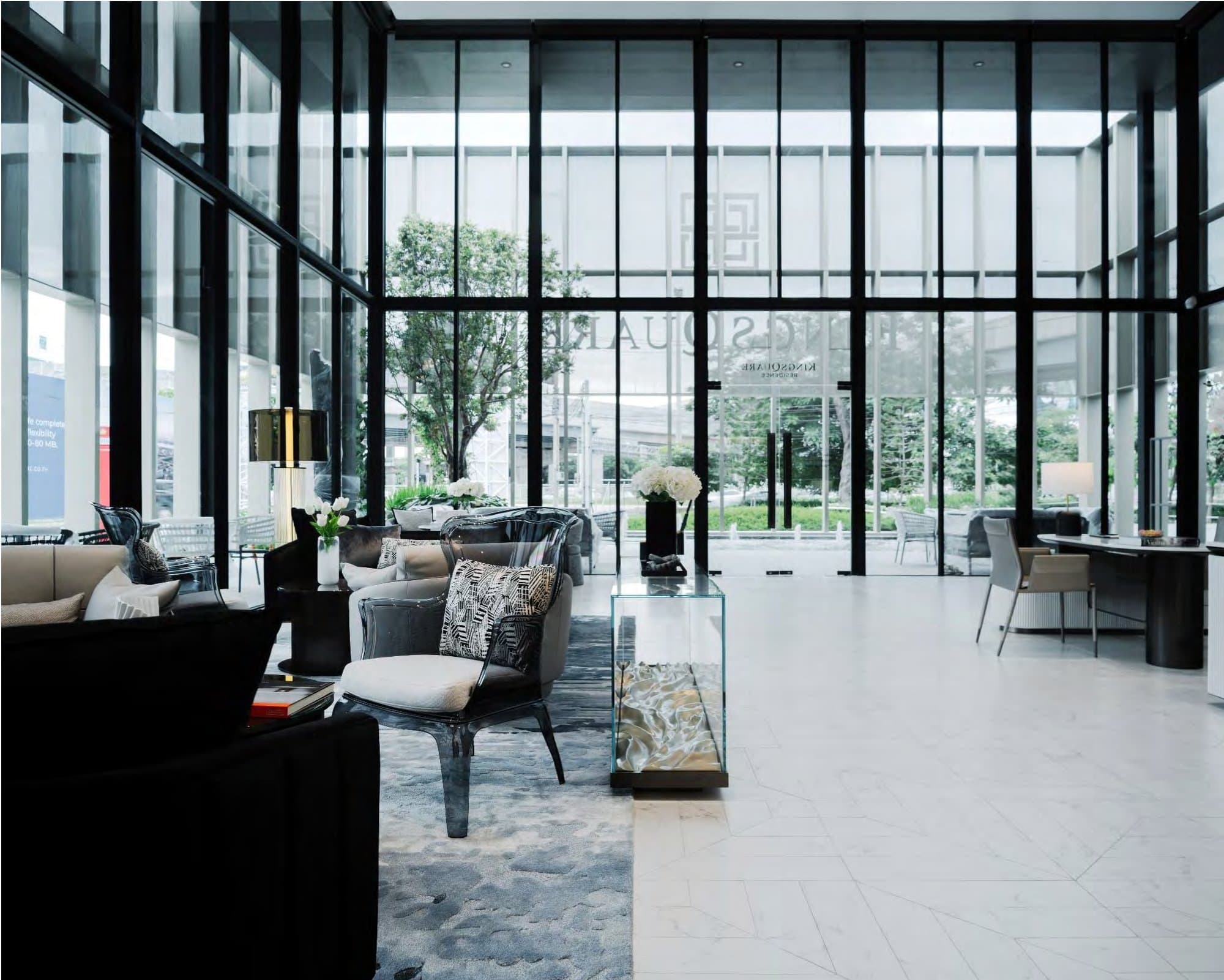 Double-height sale-gallery lobby with black-framed glazing, KINGSQUARE logo etched on glass, sculptural chairs and a garden beyond.