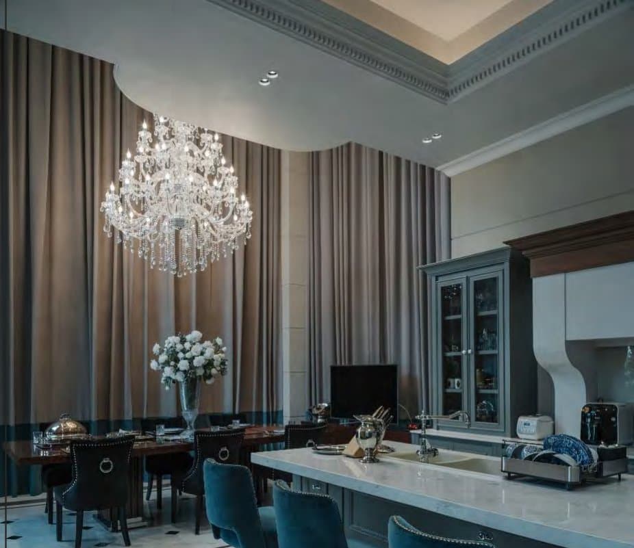 Dining area lit by a tiered crystal chandelier, studded black chairs at a dark table and floor-length taupe curtains